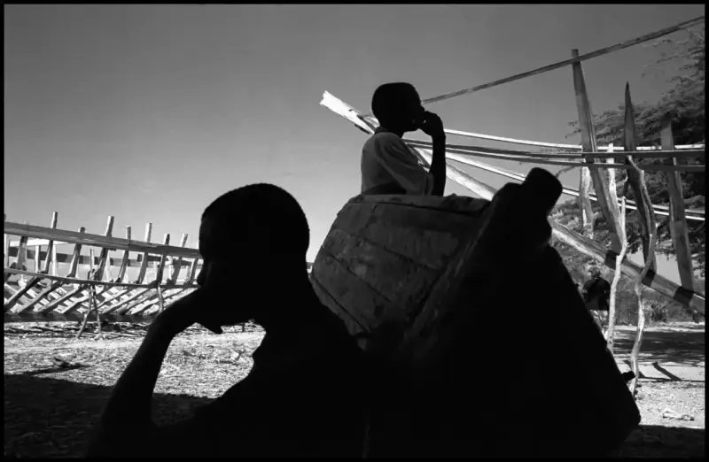 Two workers take a break from boat building in the shade. On the L'Ile de la Tortue boats are made by hand from pine trees, scrap wood and used nails and are then used in attempts to sail from Haiti to America carrying human cargo. This is the starting point for an epic voyage that many hope will take them to America. Haiti. 2000 © Christopher Anderson, Album: Christopher Anderson, Haiti. Immigrants Trip to America.